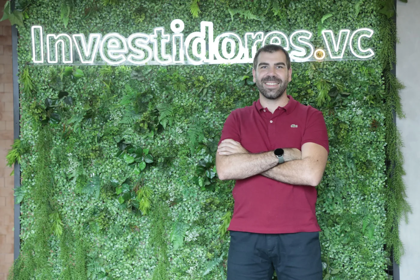 Fred Parreira de braços cruzados em frente à parede verde com o letreiro Investidores.vc